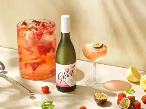En flaska vitt vin står bredvid en drink med passionsfrukt och jordgubbar. Perfekt för att drink vitt vin en solig dag.