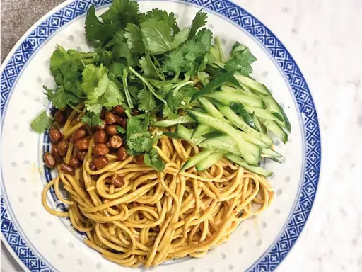 En läcker asiatisk nudelsallad med krispig gurka, rostade jordnötter och färsk koriander på en vackert mönstrad tallrik.