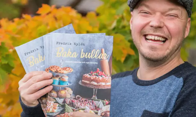 Fredrik Nylen håller upp sina böcker om kanelbullar med kardemumma, perfekt för Fredriks fika.