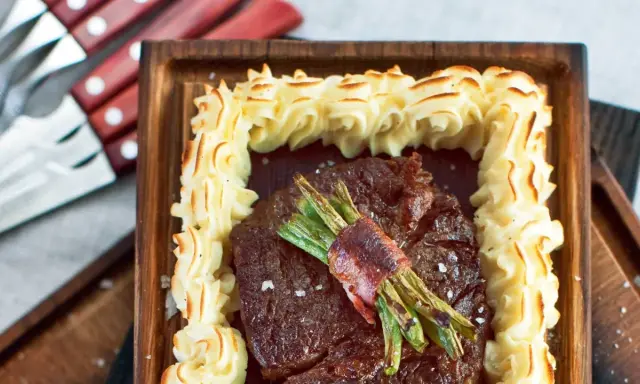 En saftig biff med sparris inslagen i bacon, omgiven av krispig potatispuré. Ett perfekt plankstek recept för en festmåltid.