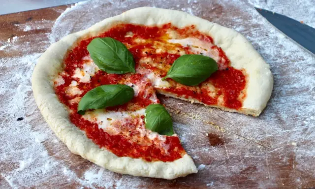 En nybakad pizza på grillen, med tomatsås, mozzarella och färsk basilika, redo att avnjutas.