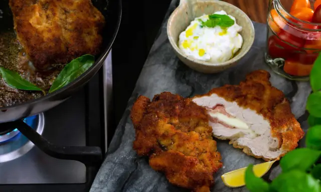 Krispig schnitzel med ost och skinka, serverad med en krämig sås till schnitzel, citron och körsbärstomater.