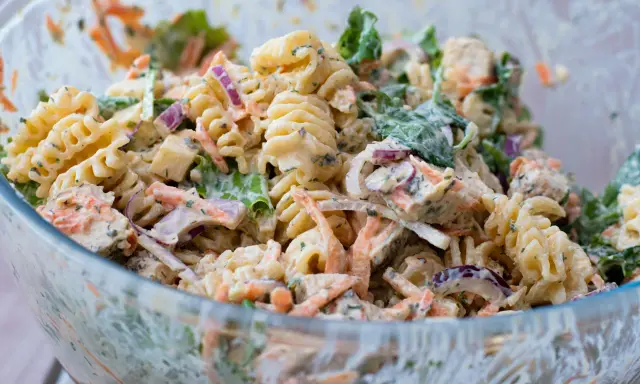 En stor skål med krämig pastasallad med kyckling, morötter, rödlök och gröna blad. Perfekt för en somrig picknick.
