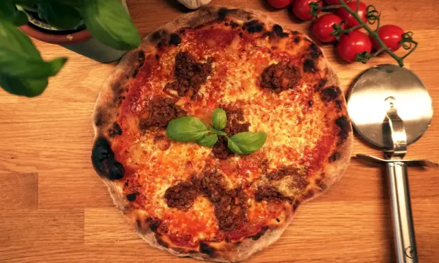En härlig napolitansk pizza med köttfärs och basilika, redo att skäras med pizzaskäraren.