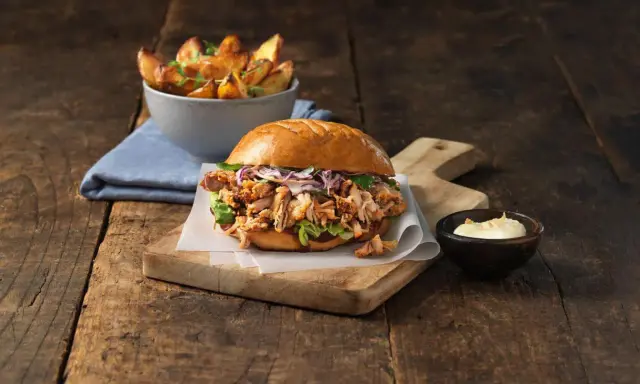 En saftig pulled pork burgare med krispig kål och en skål med ugnsrostade potatisklyftor.