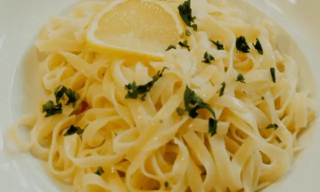 En tallrik med krämig citronpasta, toppad med en citronskiva och färsk persilja. Perfekt för en lätt lunch eller middag.