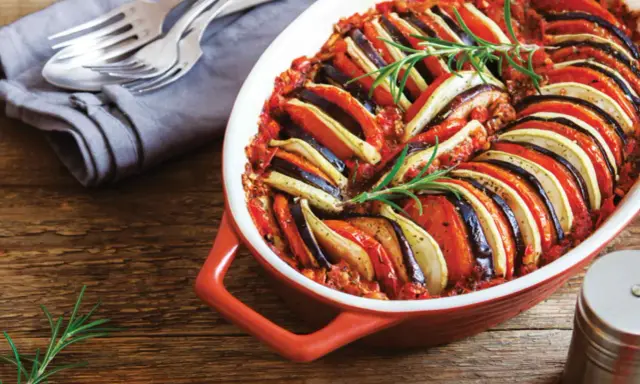 En vackert upplagd ratatouille i en ugnsform, perfekt för en nyttig middag. Grönsakerna är skivade och arrangerade i ett mönster, toppad med rosmarin.