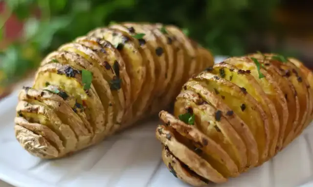 Två gyllene hasselbackspotatisar med örter, redo att serveras. Ett perfekt hasselbackspotatis recept för middagen.