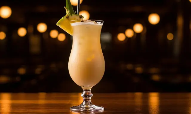 En krämig virgin piña colada, dekorerad med ananas och ett sugrör, står på en träbar med bokeh-ljus i bakgrunden.