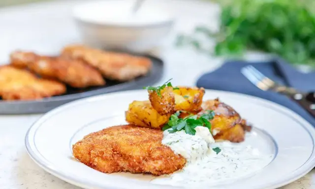 En tallrik med krispig panerad kyckling, rostade potatisklyftor och en krämig dillsås. En klassisk svensk rätt som ser utsökt ut.