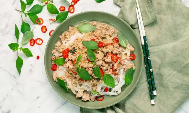 En skål med nudlar och köttfärs, toppad med färsk basilika och chili. En härlig thai mat som ser utsökt ut.