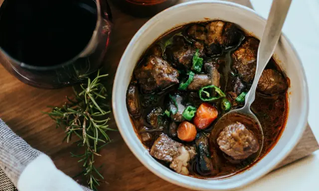En skål med mustig boeuf bourguignon, perfekt för ett mysigt recept. Serveras med en sked och en kvist rosmarin.