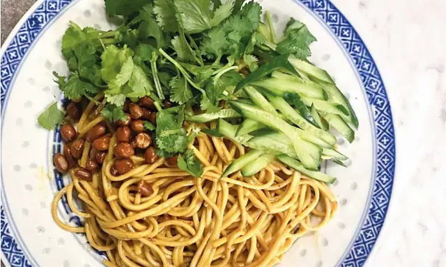 En läcker asiatisk nudelsallad med krispig gurka, rostade jordnötter och färsk koriander på en vackert mönstrad tallrik.