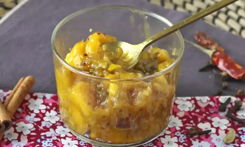 En skål med gyllene mango chutney, perfekt för ditt mango chutney recept. Kryddor som kanel och chili ligger bredvid.