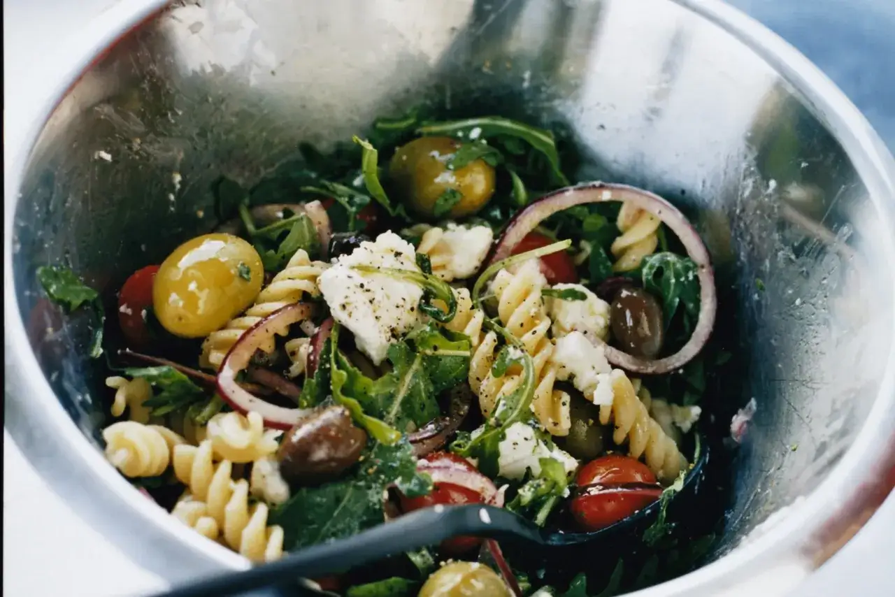 En härlig italiensk pastasallad med fusilli, oliver, tomater, fetaost och ruccola i en metallskål.