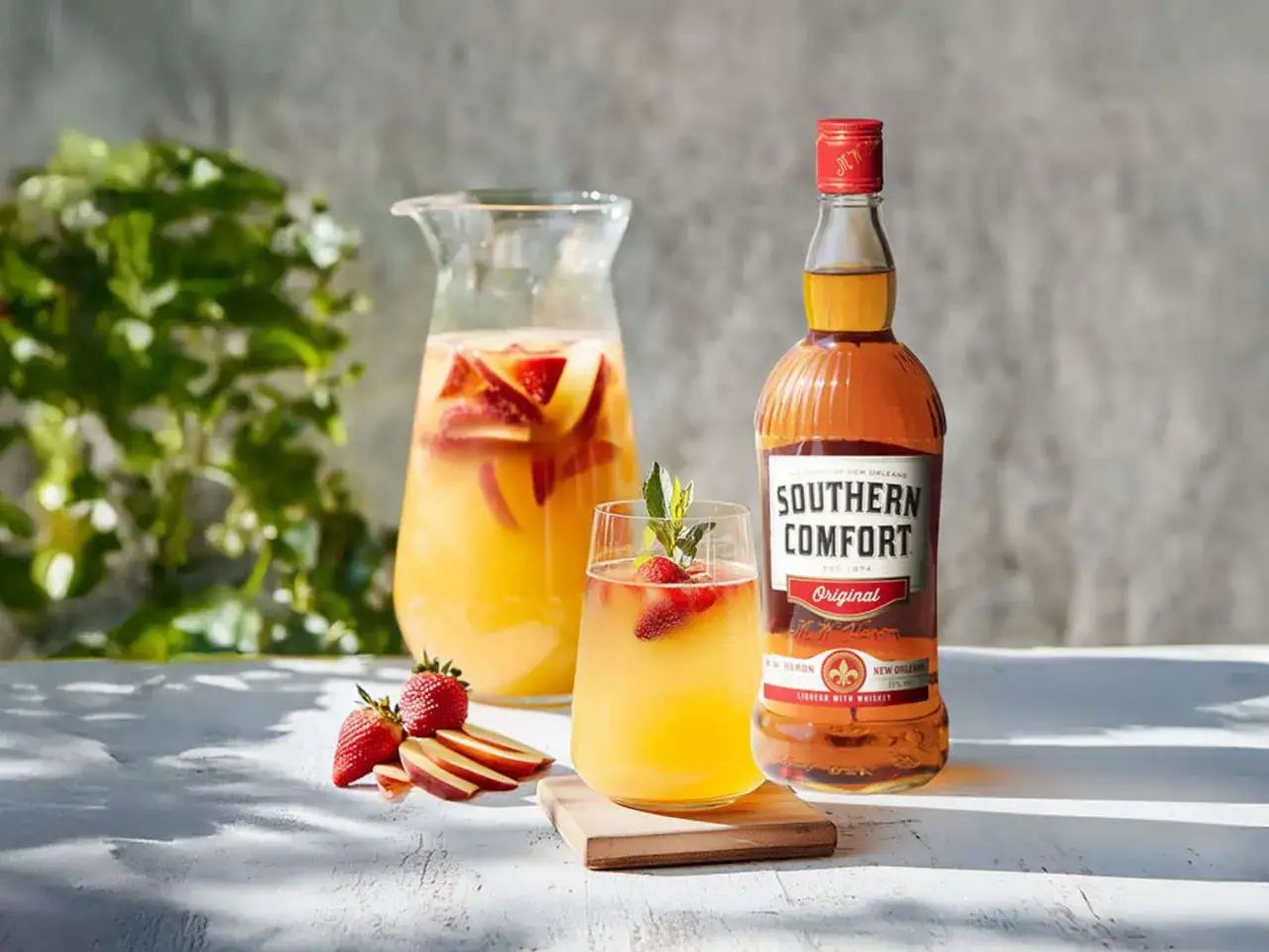 En karaff med fruktig sangria, ett glas med jordgubbar och mynta, samt en flaska Southern Comfort. Perfekt för ett somrigt sangria recept.