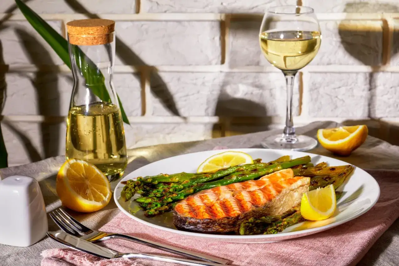 Grillad lax med sparris och citron, perfekt mat till chablis. Ett glas vitt vin står redo bredvid.