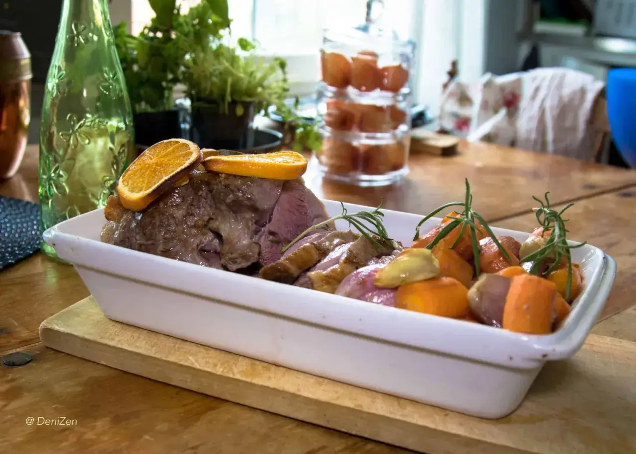 Saftig lammstek i lergryta, skivad och serverad med rostade rotfrukter och apelsinskivor.
