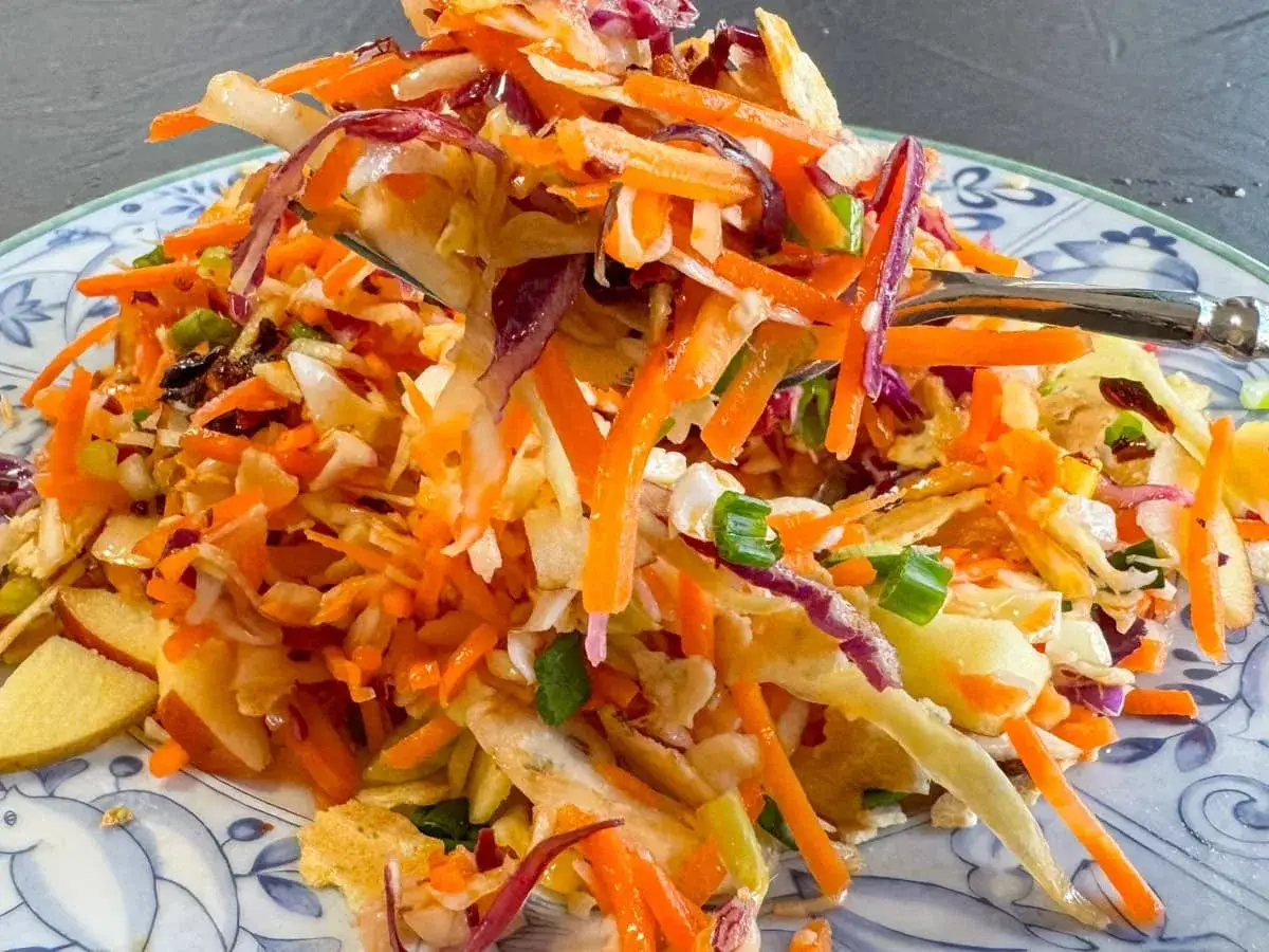 En härlig asiatisk kålsallad med strimlad vitkål, morötter, rödlök och salladslök, serverad på en blåvit tallrik.
