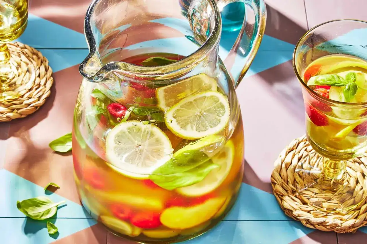 En stor karaff med vit sangria fylld med citroner, hallon och basilika. Perfekt för en solig sommardag.