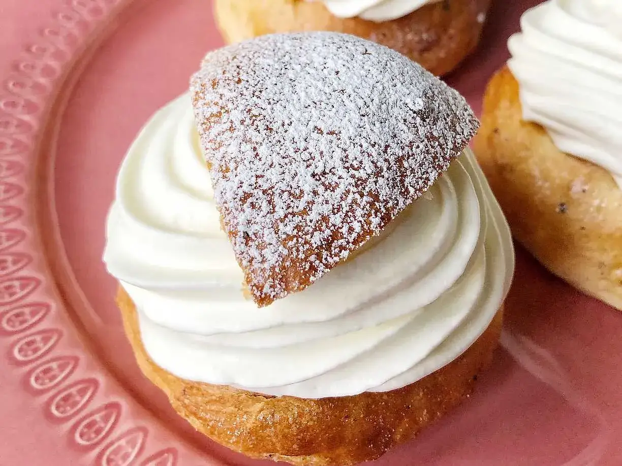 En närbild på en semla med fluffig grädde och pudersocker, perfekt för Fredriks fika. Ett klassiskt semlor recept.