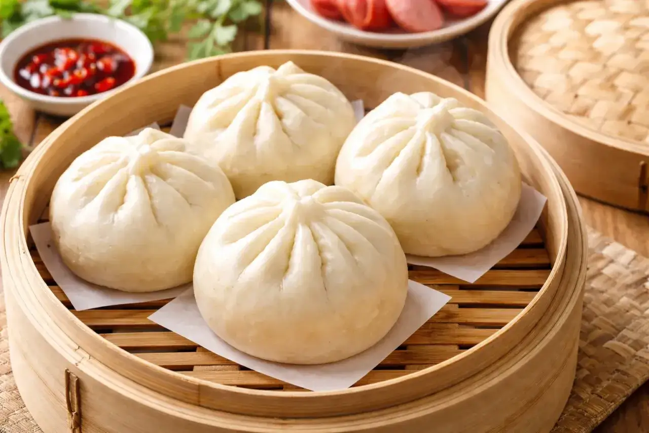 Ångkokta bao buns i bambukorg, redo att avnjutas med en kryddig dippsås.