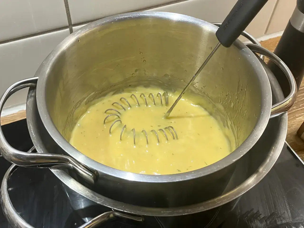 En visp rör om i en gul sås i en kastrull. Detta är ett steg i ett bearnaisesås recept.