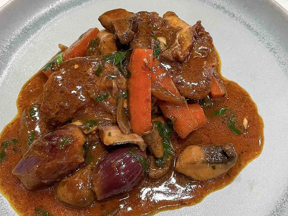 En mustig coq au vin med möra köttbitar, morötter, champinjoner och rödlök i en rik sås.