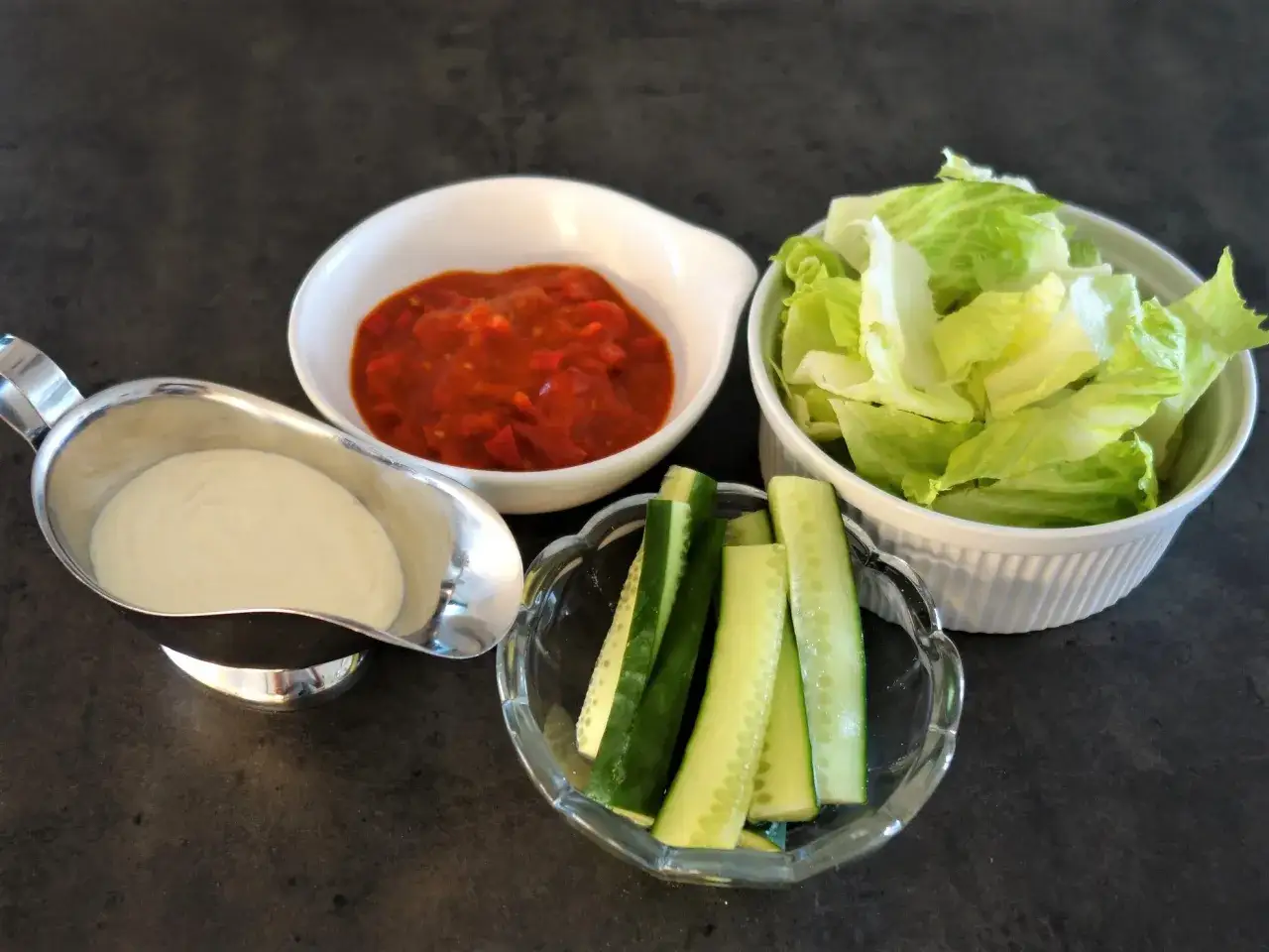 En skål med vit kebabsås, en skål med tomatsås, en skål med sallad och en skål med gurkstavar. Perfekt för ett gott kebabsås recept!