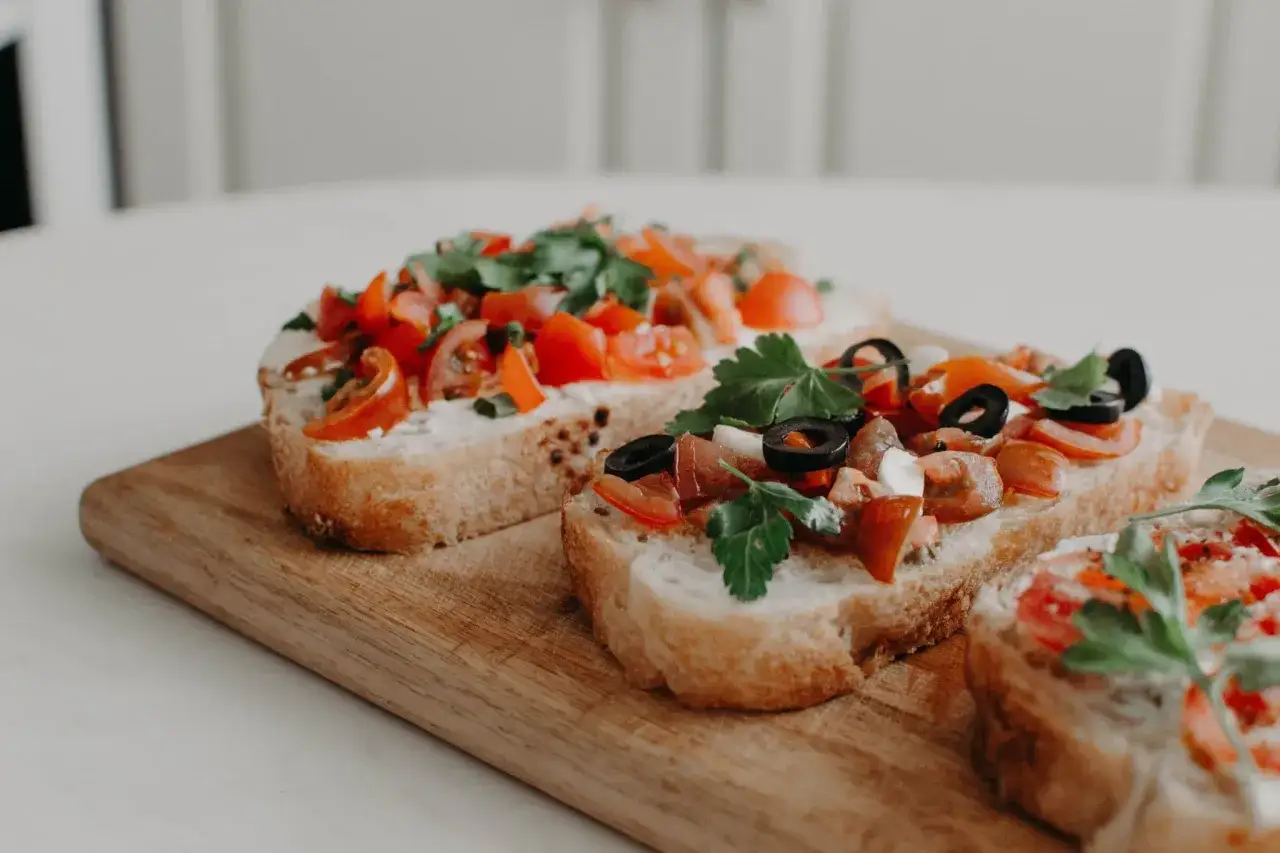 Tre läckra bruschettor med tomat, basilika och oliver på en träskärbräda. Ett perfekt bruschetta recept för sommaren.