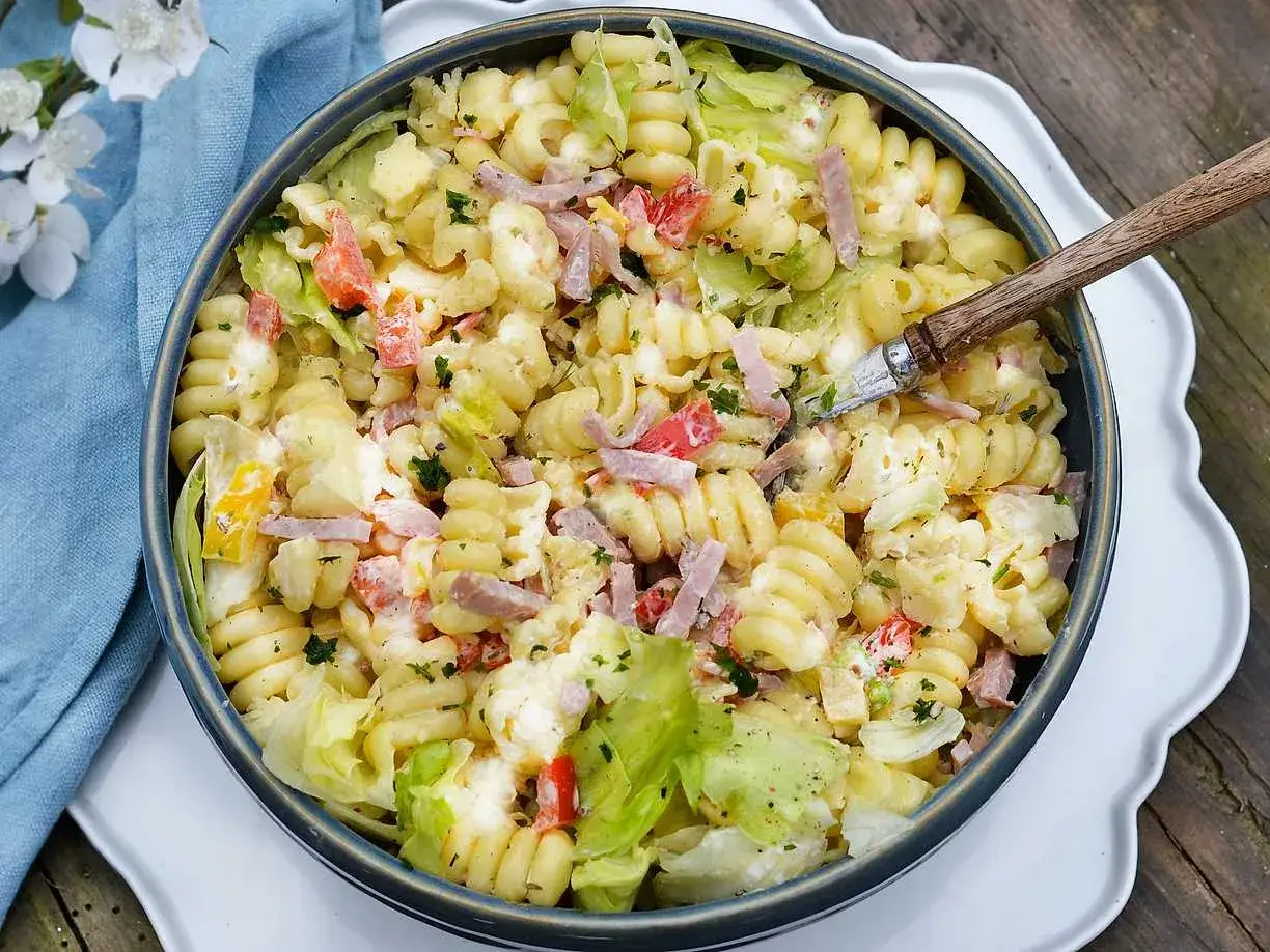 En stor skål med krämig pasta sallad med skinka, grönsaker och örter. Perfekt för en sommarlunch.