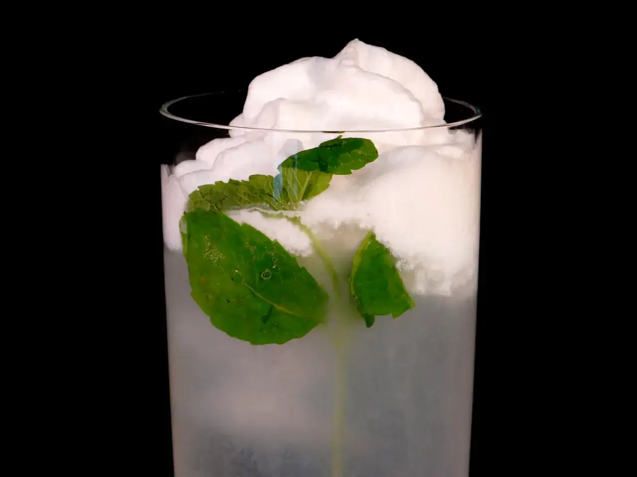 Ett glas med en uppfriskande drink med kokosskum och myntablad.