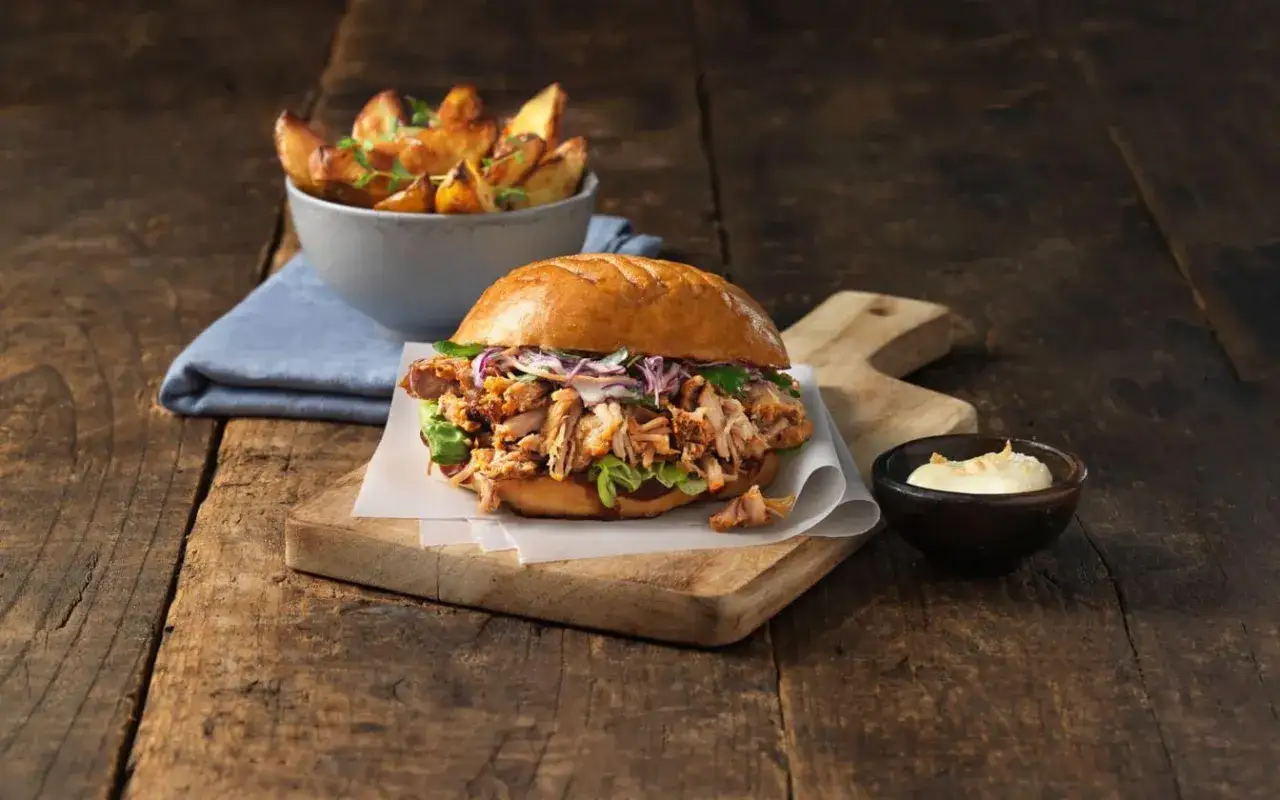 En saftig pulled pork burgare med krispig kål och en skål med ugnsrostade potatisklyftor.