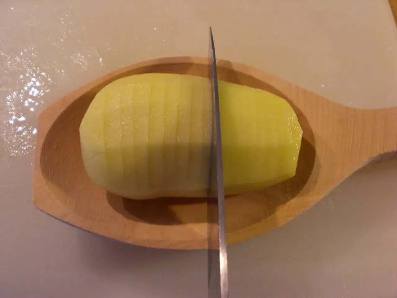 En potatis skärs i tunna skivor för ett klassiskt hasselbackspotatis recept.