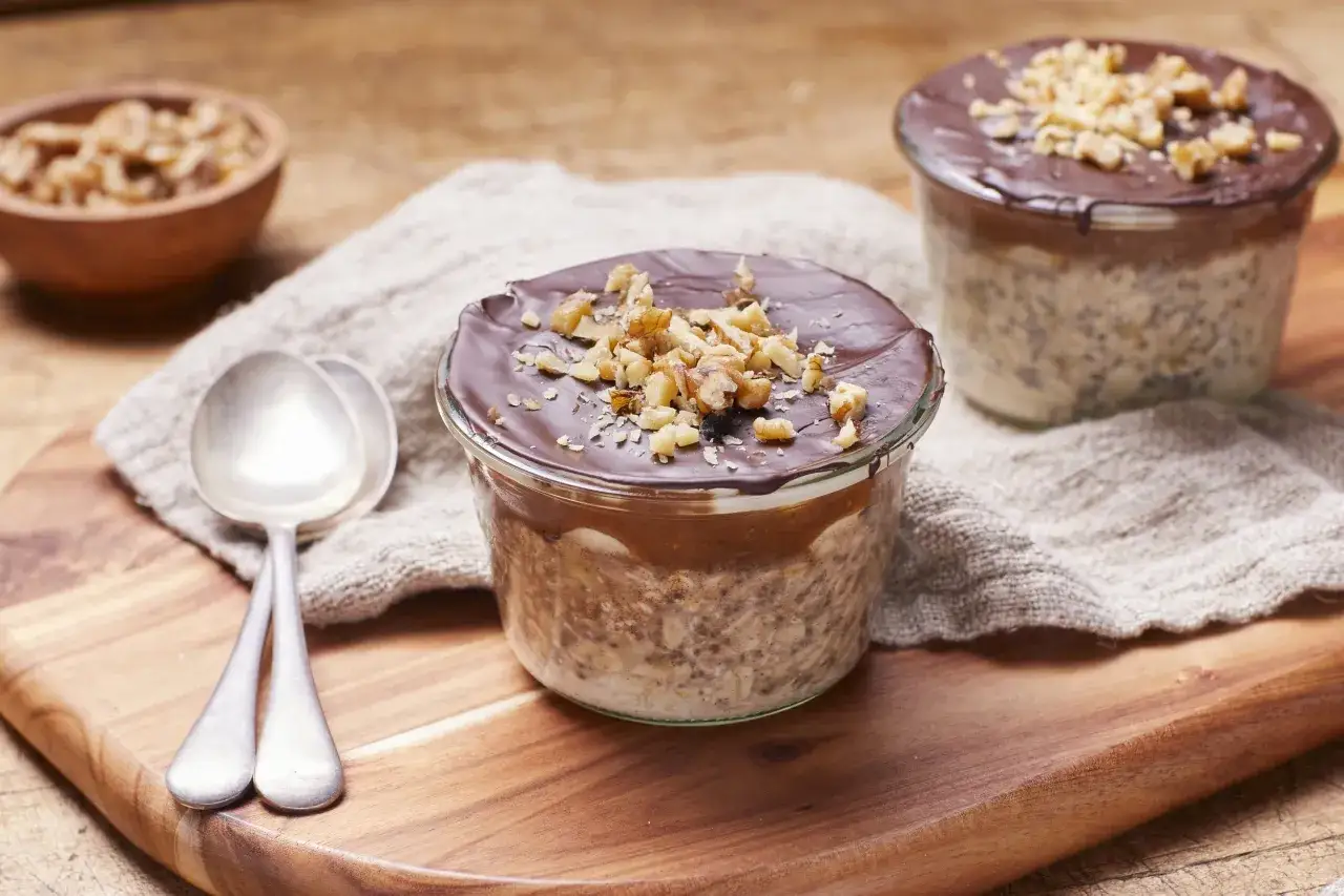 Tv&aring; glas med overnight oats choklad, toppade med n&ouml;tter och choklad. Tv&aring; skedar ligger bredvid.