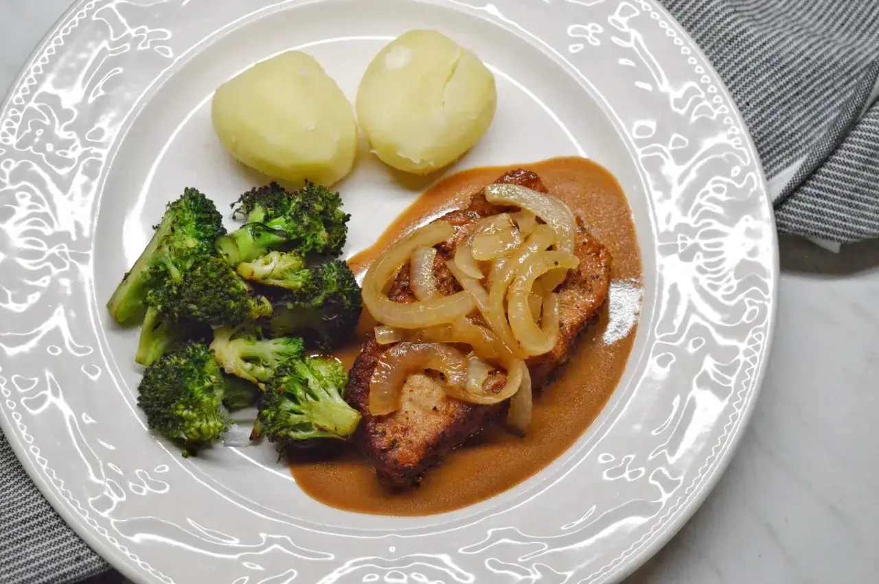 En tallrik med saftiga kotletter i ugn, serverade med krämig sås, ångad broccoli och kokt potatis. En klassisk svensk middag.