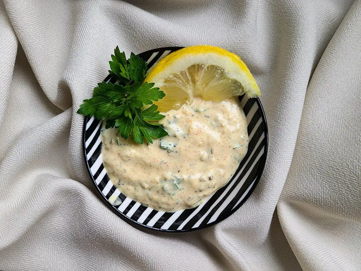 En krämig creme fraiche sås med örter och en citronskiva, serverad i en svartvit randig skål. Perfekt till sommarmaten!