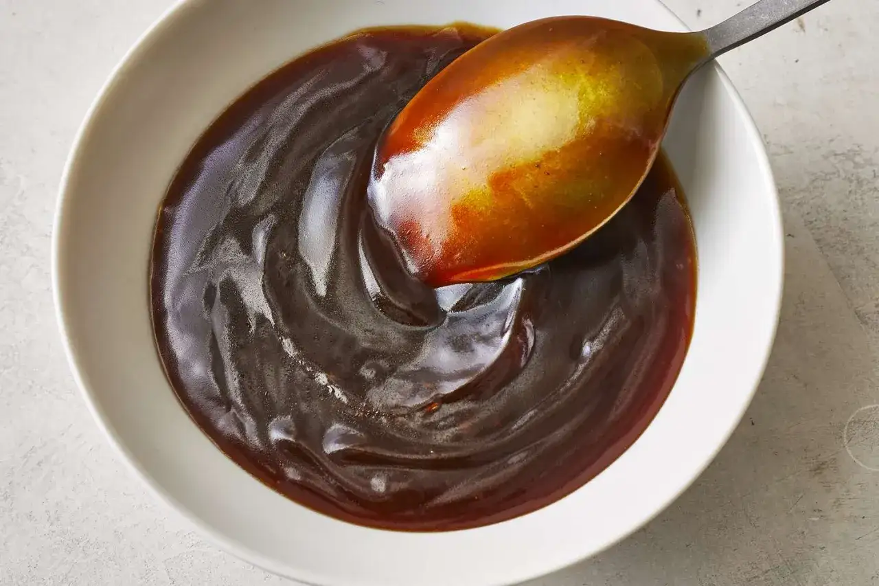 En sked lyfts ur en skål med glansig, mörk teriyakisås. Perfekt för ditt teriyakisås recept.