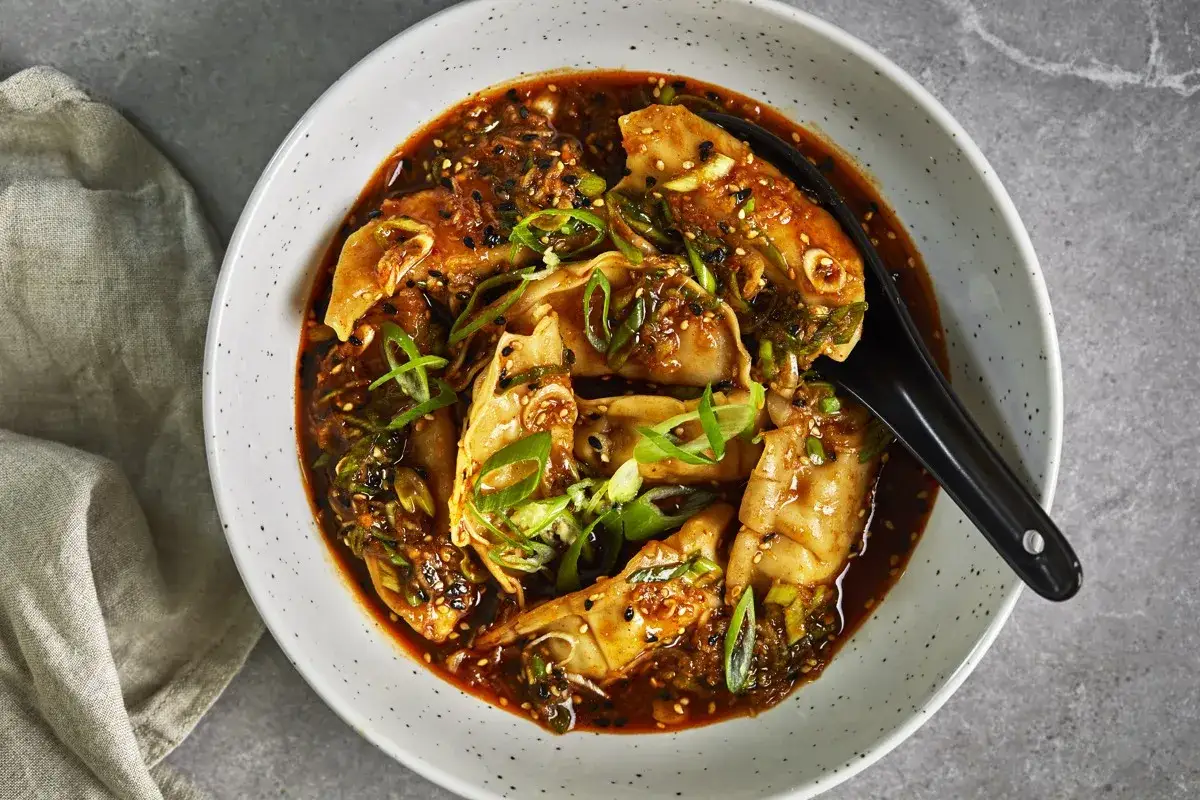 En skål med dumplings i en kryddig sås, toppad med salladslök och sesamfrön. Perfekt för en snabb middag.