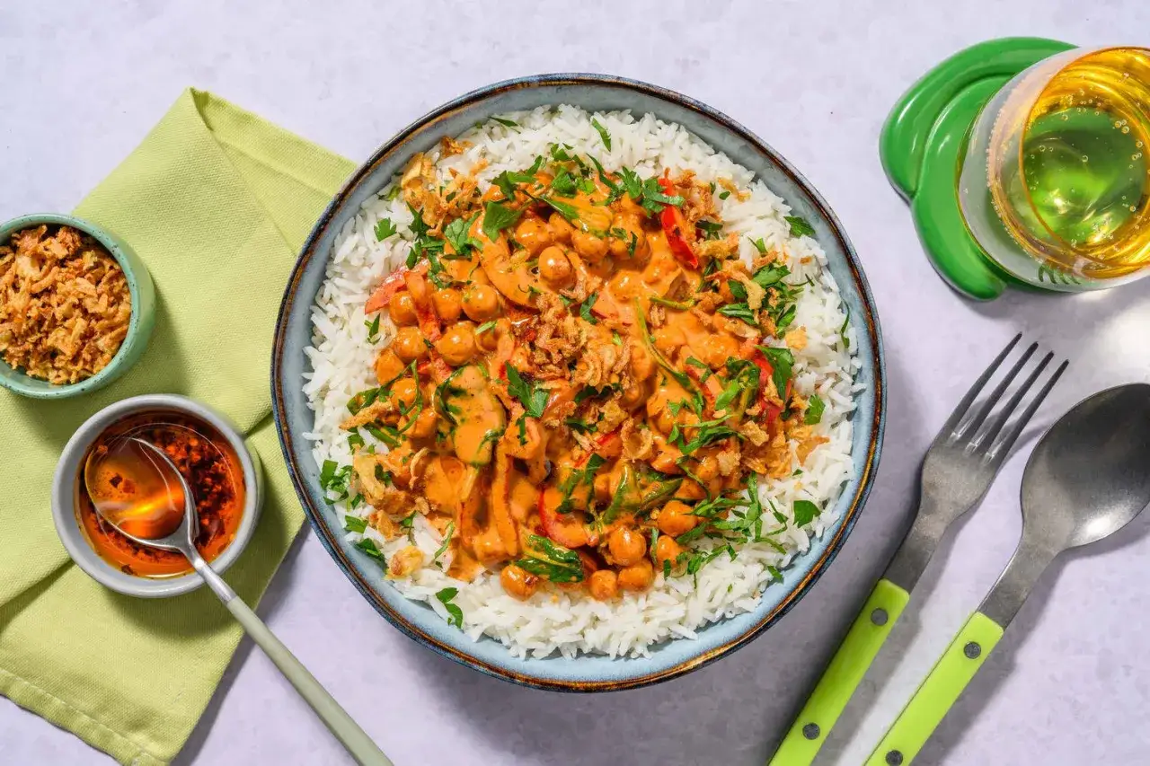 En skål med fluffigt ris toppad med en krämig kikärtscurry med paprika och toppad med krispig lök och persilja. En härlig thai mat-upplevelse!