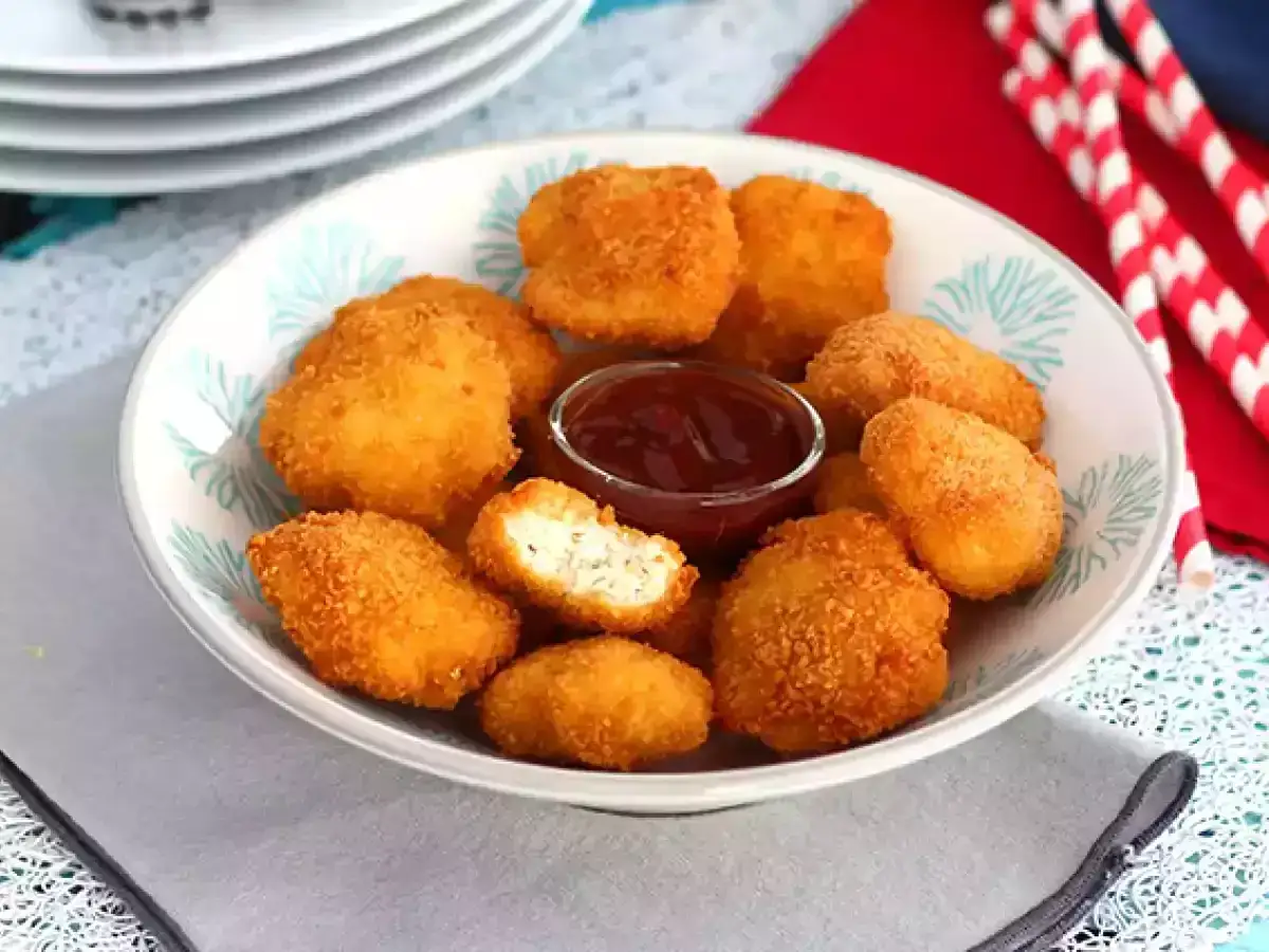 En skål med gyllene, krispiga chicken nuggets och en liten skål med barbecuesås. Perfekt för en snabb och god måltid.