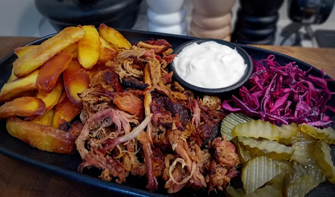 En tallrik med saftig pulled pork, gyllene klyftpotatis, krämig dipp, rödkål och saltgurka. En perfekt måltid!