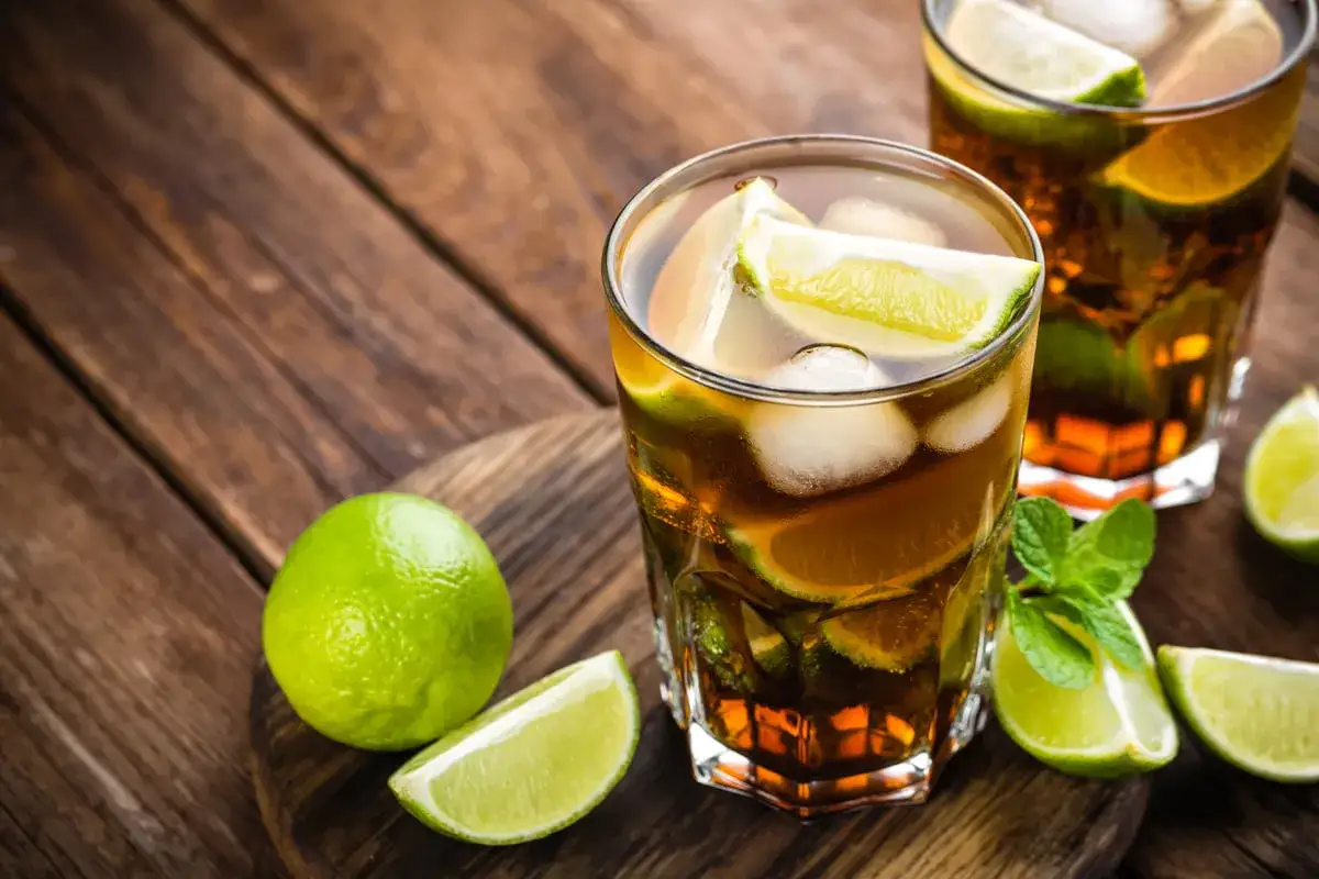 Två glas med rom och cola, is och lime. En hel lime och några limeklyftor ligger bredvid.