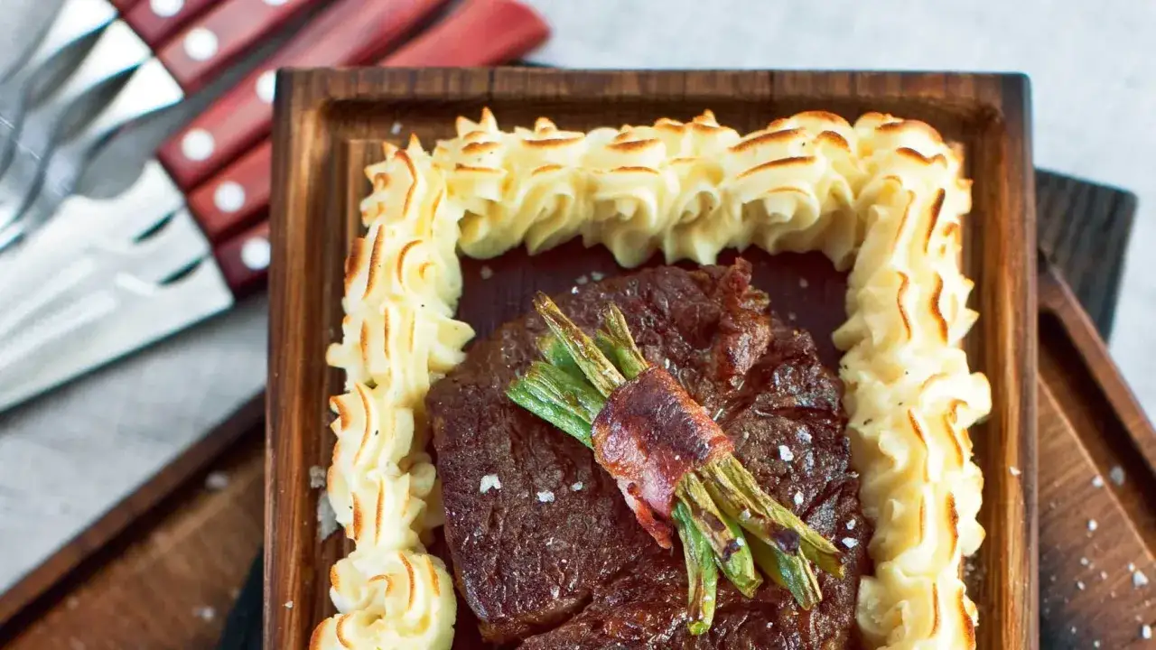 En saftig biff med sparris inslagen i bacon, omgiven av krispig potatispuré. Ett perfekt plankstek recept för en festmåltid.