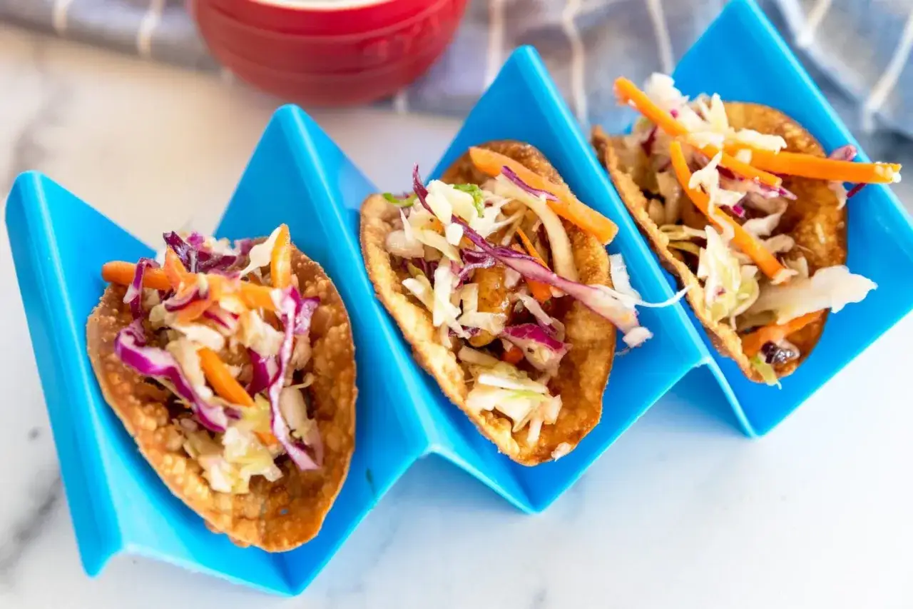 Tre läckra asiatiska tacos med krispig topping av kål och morötter i blåa hållare.