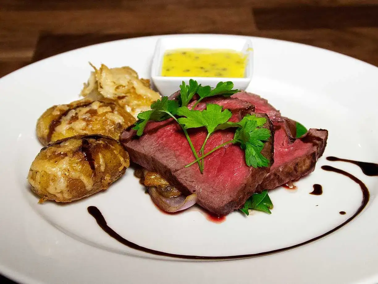 Skivat kött med rostade potatisar, en skål med sås och garnering av persilja. En svartvinbärssås dekorerar tallriken.