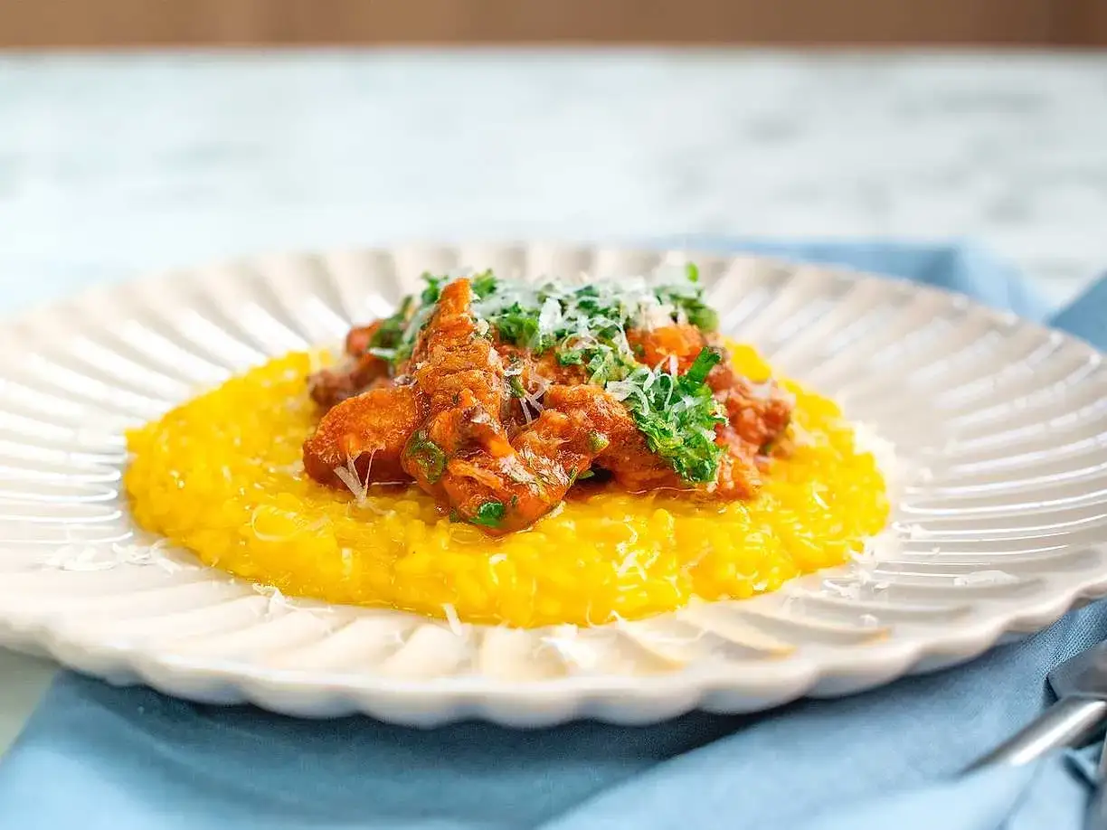 En kr&auml;mig, gul risotto toppas med en mustig gryta av osso buco, garnerad med f&auml;rsk persilja och riven parmesan.