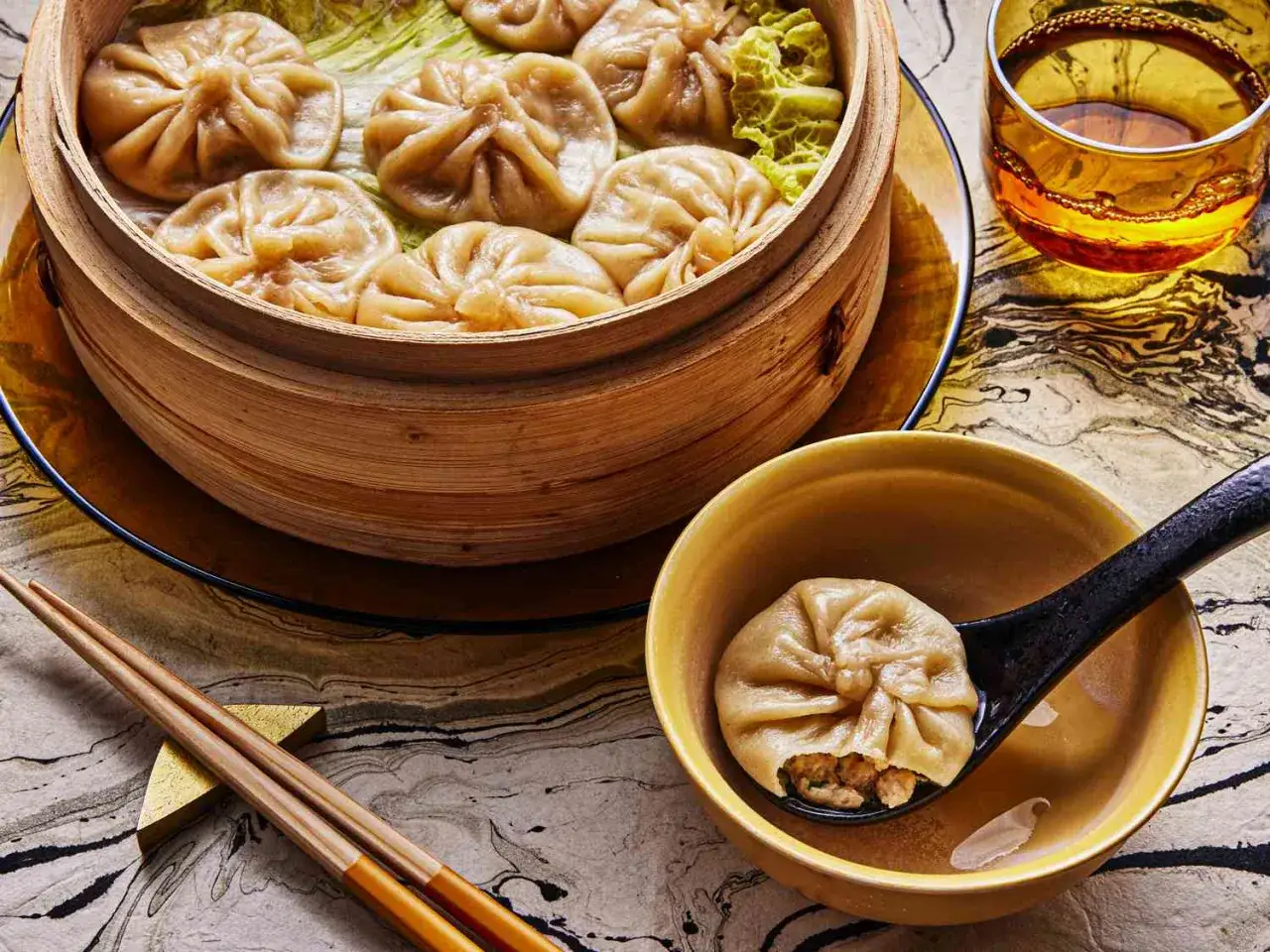 Ångkokta dumplings i bambukorg, en perfekt inspiration för ditt nästa dumplings recept. En sked visar en dumpling med fyllning.