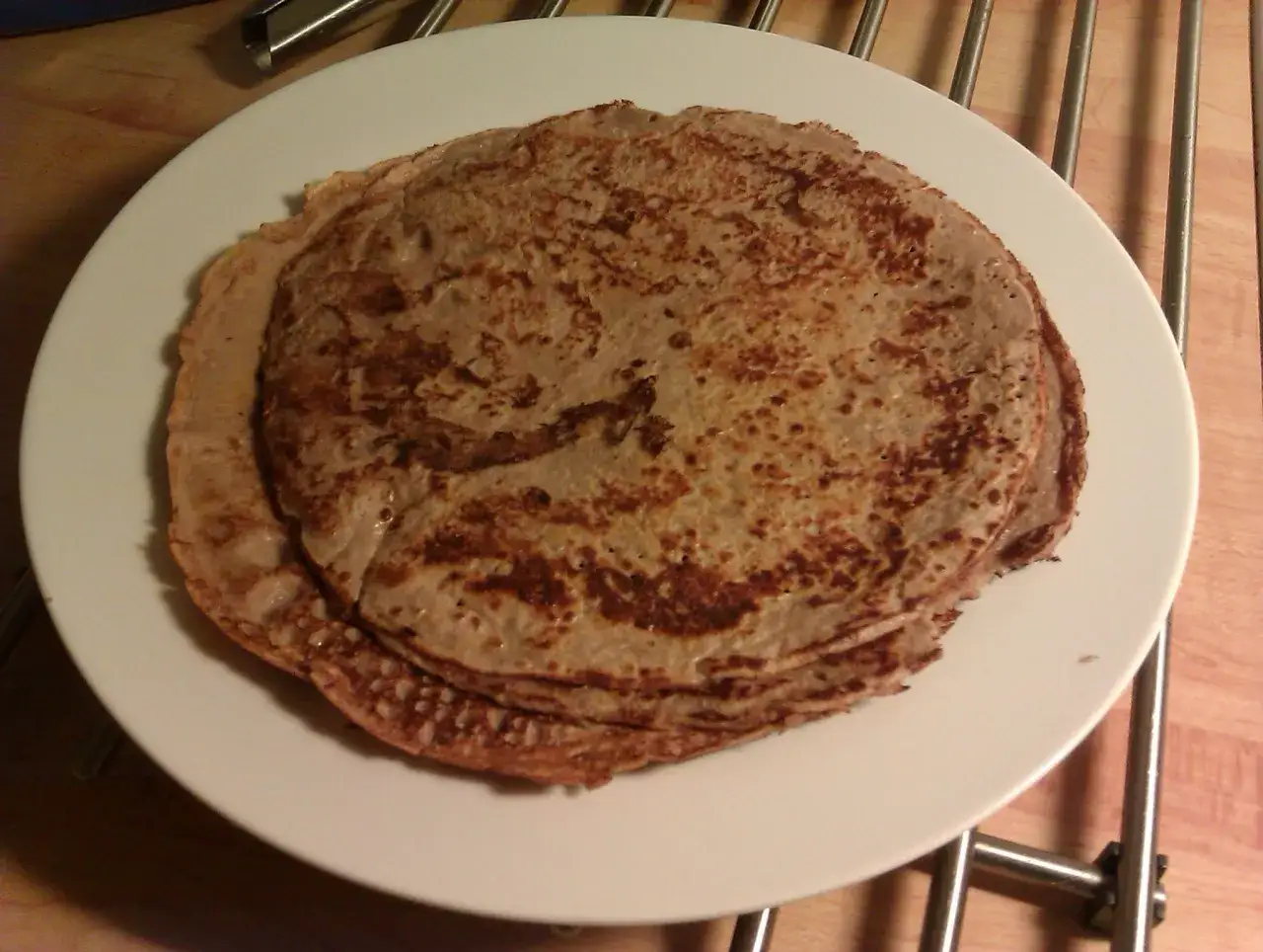 En hög med tunna pannkakor på en vit tallrik, perfekt för en proteinrik frukost.
