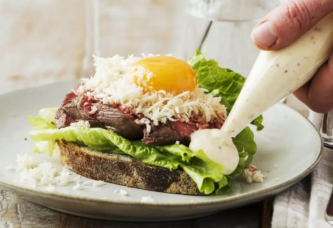 En lyxig bookmaker toast med m&ouml;rt k&ouml;tt, &auml;ggula, sallad och riven ost. En klick majonn&auml;s spritsas p&aring;.
